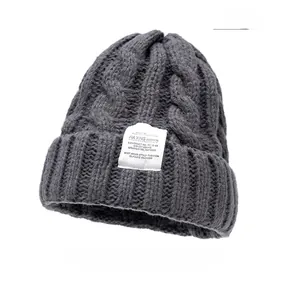 Detail of grey cable knit beanie showing thick wool texture and fashion patch label