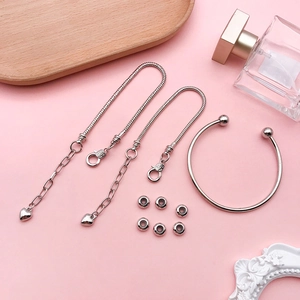 Detailed flat lay of silver DIY jewelry set with heart charm chains on pink background