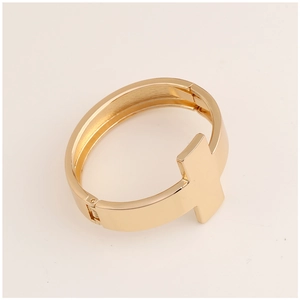 Detailed close-up of golden metal cuff bracelet featuring a raised T-shaped motif