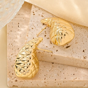 Macro detail of 14K gold plated earrings with quilted texture on natural stone and silk