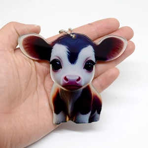 Close-up of a cartoon cow acrylic keychain with metal ball chain held by hand