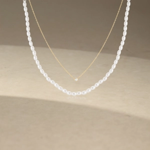 Close-up of double-layer gold chain with white rice-shaped pearls and zircon pendant