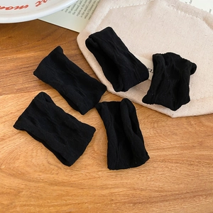 Detailed macro view of five black knitted elastic hair ties with ribbed texture on wood