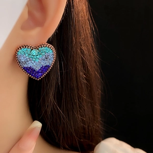 Close-up of heart-shaped earring with gradient blue crystals on a model ear lobe