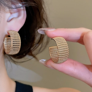 Detailed macro view of gold-plated C-shaped earrings with fine woven mesh texture