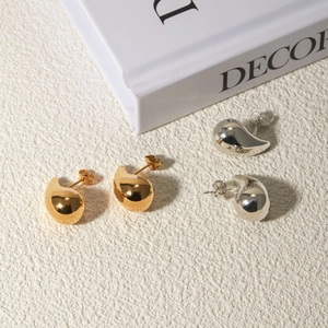 Close-up of minimalist gold and silver water drop earrings on a white decor background