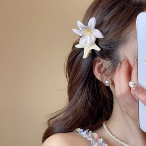 Detailed view of a white fabric flower hair clip with rhinestones worn on brown wavy hair