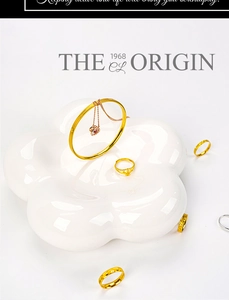 Flat lay of gold bangles, heart pendant necklace and rings on floral ceramic tray