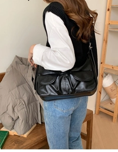 Detail of black leather shoulder bag featuring two front flap pockets in a chic style