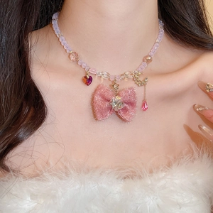 Close-up of pink bow necklace with pearls and heart charms worn by a model