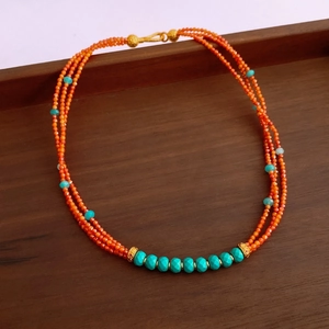Detail of three-layer beaded necklace with orange and blue beads on a wooden tray