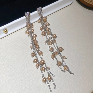 Dettaglio di orecchini a cuore in cristallo con nappe argentate e perle champagne