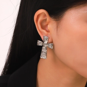 Detail shot of silver cross earrings with textured spiral pattern on a model