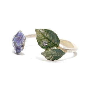 Detail of adjustable ring featuring purple enamel flower, green leaves, and a tiny zircon