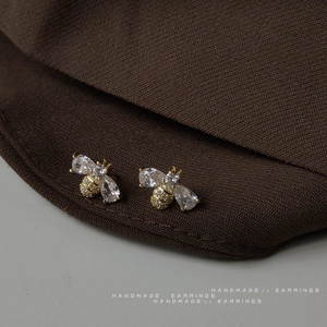 Exquisite gold bee stud earrings with micro-set zircons on a textured fabric background