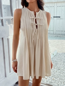 Detail of beige sleeveless pleated mini dress with lace-up front on a model in sunlight