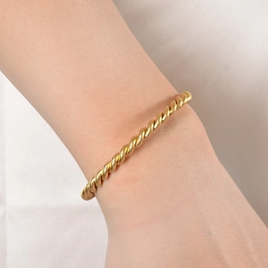 Detail of twisted rope gold cuff bracelet featuring a minimalist wave texture on wrist