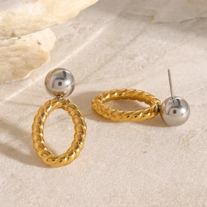 Macro detail of geometric earrings featuring gold twisted ring and silver ball stud