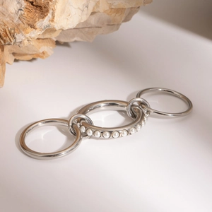 Detail of silver layered interlocking rings with pearl accents on a minimalist background