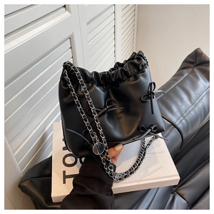 Detail of black leather bucket bag with ribbon bow and silver chain strap on books