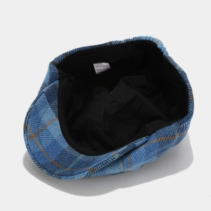 Detail view of plaid newsboy cap interior showing the black lining and material tag
