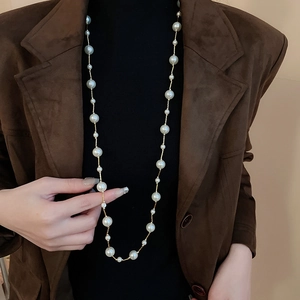 Detail of long layered artificial pearl necklace on a brown suede jacket and black turtleneck