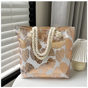 Detail of canvas tote bag with golden leaf pattern and braided rope handles in natural light