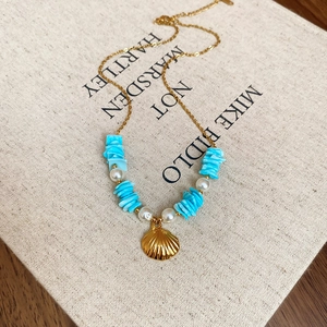 Macro shot of seashell pendant and blue stones on gold chain with pearl accent