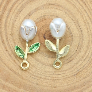 Macro shot of tulip charms with white pearls and green enamel on a wood surface
