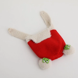 Detail of red knit baby winter hat with cute green frog embroidery and plush ear flaps