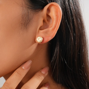Close-up of golden metal woven knot stud earring worn by model with high gloss finish