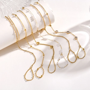 Detailed view of gold finger bracelets with heart and pearl charms on white display