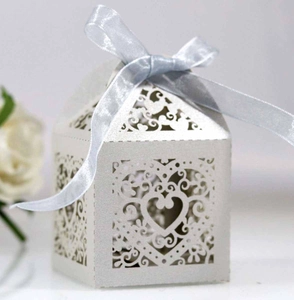Close-up of white laser-cut heart pattern wedding favor box with a blue ribbon bow