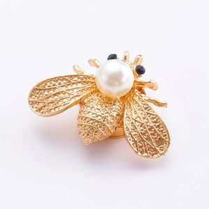Détail d'un clip de vêtement abeille dorée avec perle blanche et strass noirs incrustés
