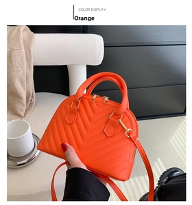 Detail of orange quilted shell handbag with gold zippers and detachable shoulder strap