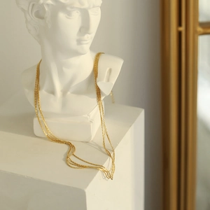 Artistic detail of multilayered gold snake chain necklace draped on a white plaster bust