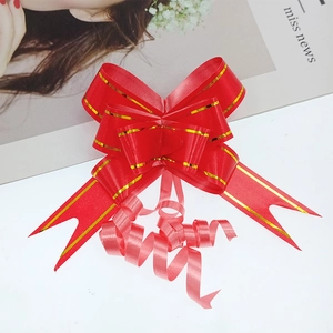 Detail of red gift bow with gold edges and curled ribbon tails on a white decorative card