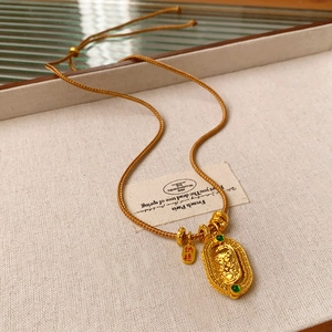 Macro shot of gold woven necklace featuring green gemstone pendant and lucky charm