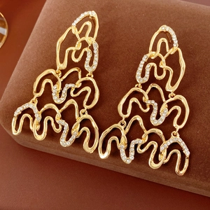 Detailed view of gold wavy earrings with white rhinestones on brown velvet surface