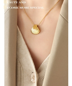 Detail of a gold shell pendant necklace with striped texture on a model's neck