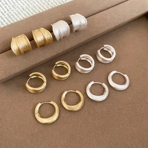 Elegant matte gold and silver brushed metal hoop earrings on a velvet display stand