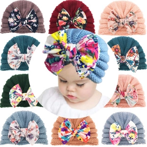 Close-up of elastic knitted baby hats featuring oversized floral printed bow decorations