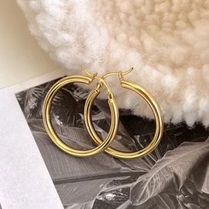 Close-up of elegant gold hoop earrings on soft white fabric background with artistic prints