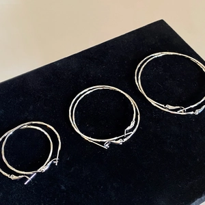 Macro detail of three pairs of silver twisted hoop earrings on black velvet stand