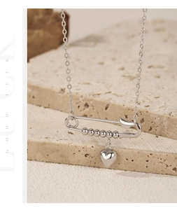 Detailed view of silver heart pendant and safety pin necklace on a travertine stone
