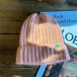 Close-up of pink ribbed knit beanie featuring an embroidered patch on a wooden surface