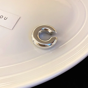 Vue macro d'un earcuff en argent sur céramique blanche, finition polie au style épuré