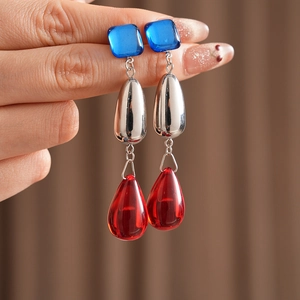 Close-up of vintage earrings featuring blue square and red teardrop gemstones held in hand