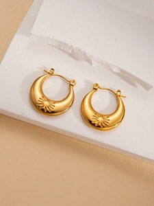 Macro detail of gold-plated crescent earrings with sunburst texture on a stone plate