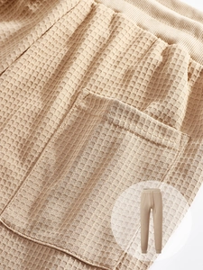 Detailed macro view of waffle knit fabric texture and side pocket stitching on camel joggers
